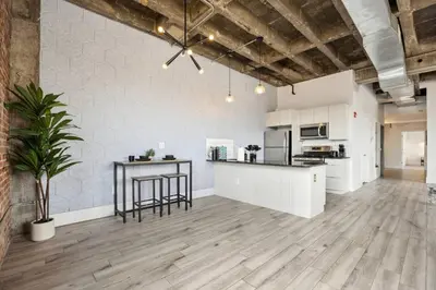 an open kitchen and living room with white cabinets at Lofts at Kearny - Rustic Chic 1-3BR Lofts with Quick NYC Access & On-Site Gym in Kearny