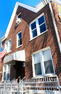 a red brick building with a white fence in front of it at NYC cozy room in Van Nest