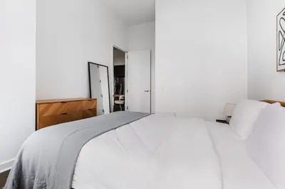 a white bedroom with a white bed and a mirror at Blueground Midtown S gym AC nr Empire St NYC-1591 in New York