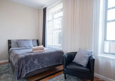 a bedroom with a bed and a chair and a window at 3BR apt two blocks to Central Park elevator, laundry, virtual doorman in New York