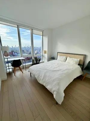 a white bedroom with a bed and a desk and windows at 1 Stop to Midtown Amazing View Luxury High Rise Corner 1 Bedroom Apartment in Sunnyside