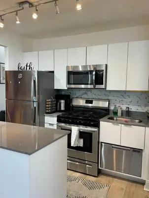 a kitchen with stainless steel appliances and white cabinets at NEW Modern 2BR w Fireplace & Fitness Lounge, Live Comfortably in East Harlem in New York