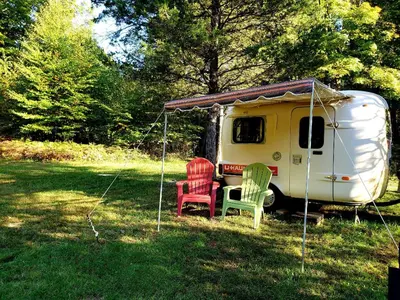 a caravan with two chairs and a tent in the grass at Unique Caravan for Vintage Glamping Experience in Pine Bush, New York in Pine Bush