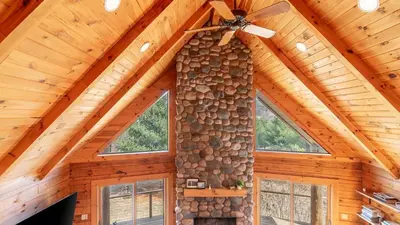 a ceiling fan in a log cabin with a fireplace at Secluded w Deck Views Hot Tub Ping Pong Hudson in the Berks by AvantStay in East Chatham