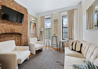 a living room with white furniture and a brick fireplace at Upper West Side Furnished 1 Bedroom Apartment, June to Aug 90 days stay required in New York
