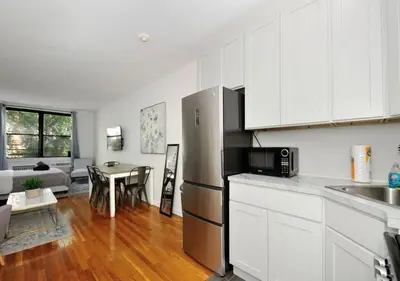 a kitchen with a stainless steel refrigerator and a table at Charming UES Studio, Walk to Subway & Central Park, June To Aug 90 Days Stay Required in New York
