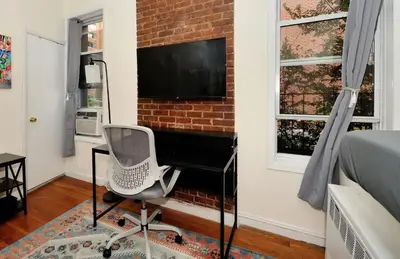 a bedroom with a desk and a television on a brick wall at Amazing Upper East Side Studio! Epic Location!, June To Aug 90 Days Stay Required in New York