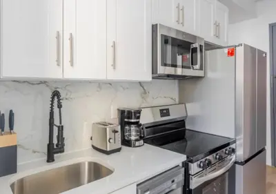 a kitchen with white cabinets and a stainless steel refrigerator at Murray Hill 1 Bed Furnished Apt in New York