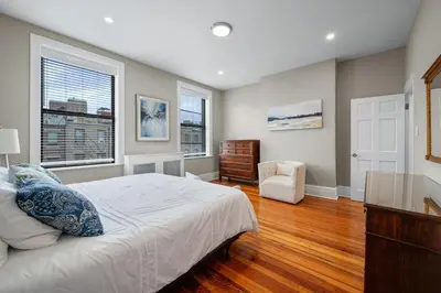 a bedroom with a bed and a chair and two windows at Luxury Townhouse in NYC in New York