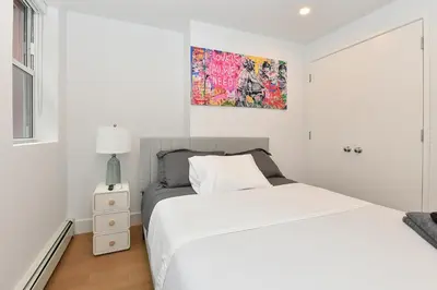 a white bedroom with a bed and a painting on the wall at Sophisticated 3 Bedroom Duplex in the Heart of Midtown in New York