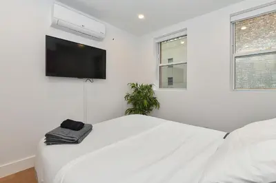 a white bedroom with a bed and a flat screen tv at Sophisticated 3 Bedroom Duplex in the Heart of Midtown in New York