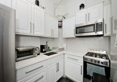 a white kitchen with white cabinets and a microwave at 1BR GEM! Close to Central Park!, June To Aug 90 Days Stay Required in New York