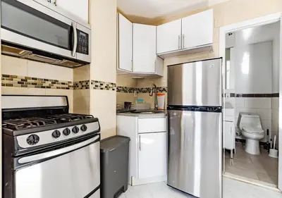 a kitchen with white cabinets and a stainless steel refrigerator at Spacious Upper East Side Studio, June To Aug 90 Days Stay Required in New York