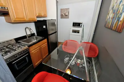 a kitchen with a stove and a sink and red chairs at Furnished 2 Bedroom Apartment in Lennox Hill, June To Aug 90 Days Stay Required in New York