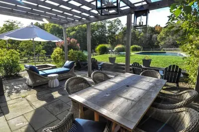 a wooden table with chairs and an umbrella on a patio at Haddock Cotter Chic Farmhouse and Barn w Pool in Old Chatham
