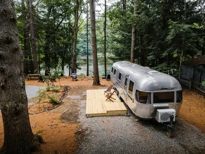 a person sitting on a wooden platform next to a trailer at Waterfront, Pet Friendly Airstream near Lake George in the Adirondack, New York in Corinth