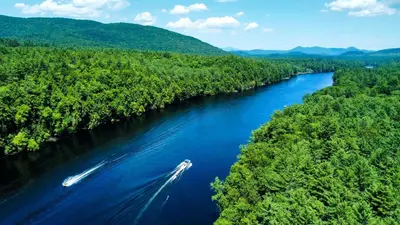 a boat traveling down a river in the woods at Luxury Group Safari Tent Complete with Firepit and Patio, Perfect for a Weekend Escape to the Adirondacks in Corinth