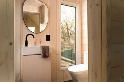 a bathroom with a toilet and a mirror and a window at Secluded, Dog Friendly Tiny House on the Hudson River, near Saratoga Springs in Corinth