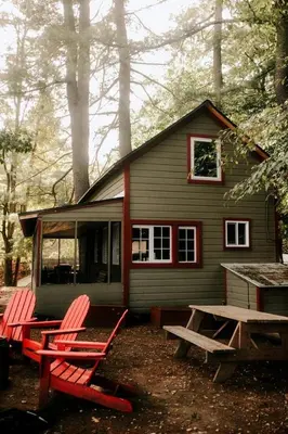 two red chairs and a picnic table in front of a house at Rustic, Pet Friendly Cabin on the Hudson River, Perfect for a Glamping Weekend in the Adirondacks in Corinth