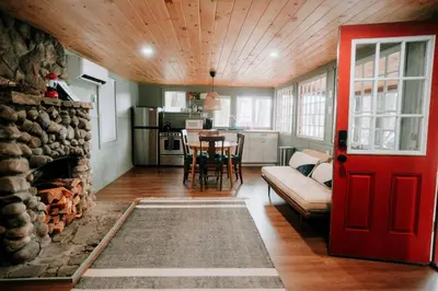 a living room with a red door and a fireplace at Rustic, Pet Friendly Cabin on the Hudson River, Perfect for a Glamping Weekend in the Adirondacks in Corinth