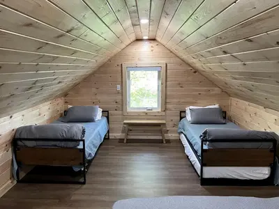 two beds in a log cabin with a window at Rustic, Pet Friendly Cabin on the Hudson River, Perfect for a Glamping Weekend in the Adirondacks in Corinth