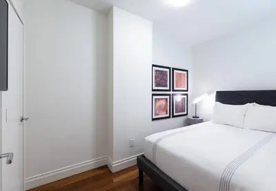 a white bedroom with a bed and two pictures on the wall at 3BR Apartment in Big Apple in New York