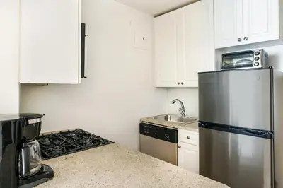 a kitchen with white cabinets and a stainless steel refrigerator at Lovely and Comfy Studio in NYC in New York