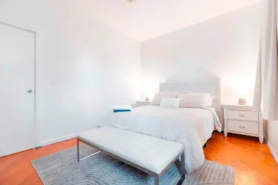 a white bedroom with a white bed and a bench at Prime Location Upper Manhattan Furnished Apartment in New York