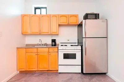 a kitchen with orange cabinets and a refrigerator at Prime Location Upper Manhattan Furnished Apartment in New York