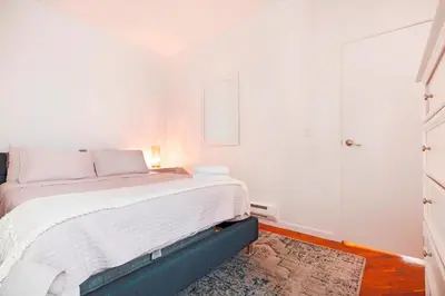 a white bedroom with a large bed with white sheets at Prime Location Upper Manhattan Furnished Apartment in New York