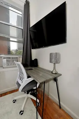 a desk with a chair and a television on a wall at Cozy Studio Steps to Central Park Upper E Side in New York