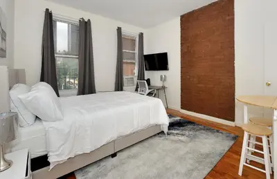a bedroom with a white bed and a brick wall at Cozy Studio Steps to Central Park Upper E Side in New York