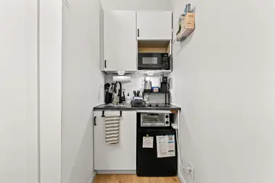 a small kitchen with white cabinets and a black refrigerator at Micro Studio Walk to Time Square in New York