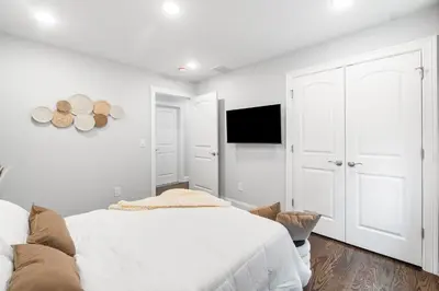 a white bedroom with a bed and a flat screen tv at Orange's Oasis in East Orange