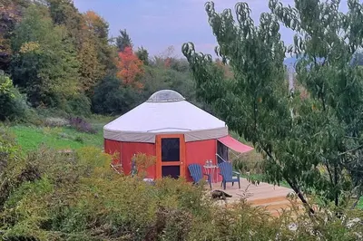 a red tent with a table and chairs in a field at Modern Countryside Yurt Rental in Waterville, Upstate New York in Waterville