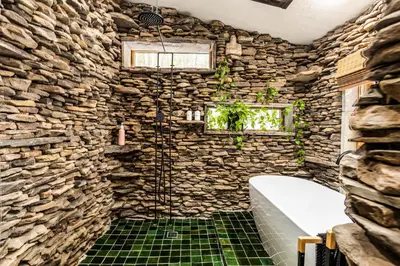 a stone walled bathroom with a tub and a window at Stunning Catskills Cabin in Margaretville
