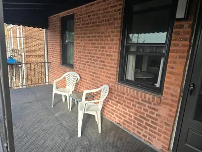 two white chairs sitting next to a brick wall at Astoria, steps away from Manhattan in Astoria