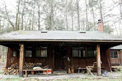 a wooden cabin with a pile of fire wood at Rustic Cabin Retreat on the Ten Mile River in Narrowsburg, New York in Narrowsburg