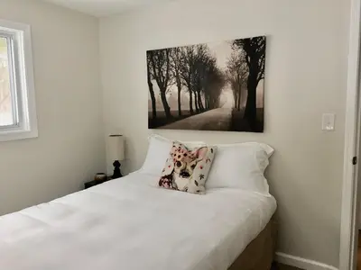 a bedroom with a white bed with a painting on the wall at Beautiful Lakefront Chalet in the Poconos! in Hawley