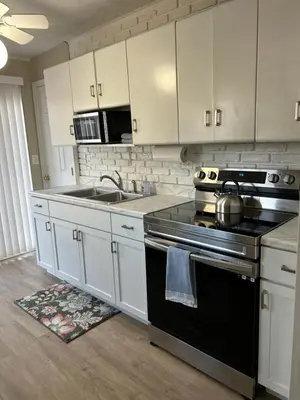 a kitchen with white cabinets and a stove and a sink at Charming Cottage with fenced yard in convenient location in Longmeadow