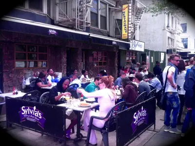 a group of people sitting at tables outside a restaurant at Top Rated 1BR - Lenox 127 in New York