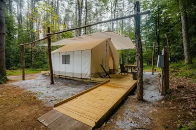 a tent with a wooden deck in the woods at Classic Safari Tent in the Heart of the Adirondack Wilderness, near Lake George, New York in Corinth