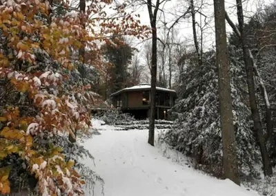 a snow covered path leading to a cabin in the woods at Imaginative Octogonal Glass Treehouse on Seven Private Acres near Great Barrington, MA in Great Barrington