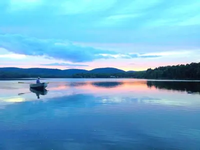 a person in a boat on a lake at sunset at Charming Cabin with Serene Lake Views for a Family Getaway near Pittsfield, Massachusetts in Pittsfield