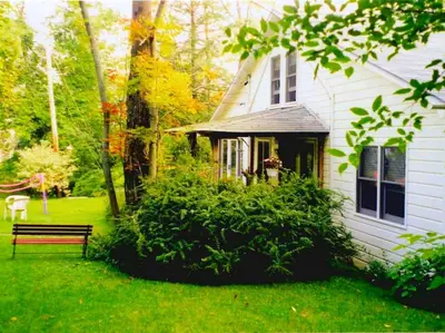 a white house with a bench in the yard at Charming Cabin with Serene Lake Views for a Family Getaway near Pittsfield, Massachusetts in Pittsfield