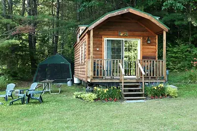 a wooden cabin with a porch and a tent at Deluxe Vacation Cabin Rentals in the Adirondacks near Saratoga Springs, New York in Corinth