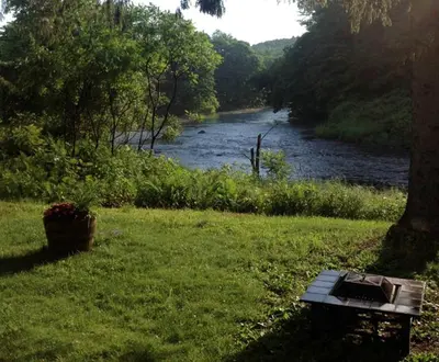 a bench sitting in the grass next to a river at Secluded Cabin with Gorgeous Views near Stockbridge in the Berkshires of Massachusetts in Stockbridge