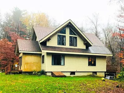 a yellow house on a green field with trees at Beautiful Two-Bedroom Cabin Rental Set in the Forests of the Berkshires, Massachusetts