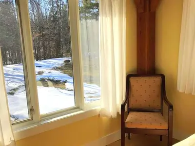 a chair sitting in front of a window with snow at Beautiful Two-Bedroom Cabin Rental Set in the Forests of the Berkshires, Massachusetts