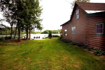 a house with a grass yard next to a lake at Lakefront Cabin Getaway near Adirondack Mountains in Salisbury, New York